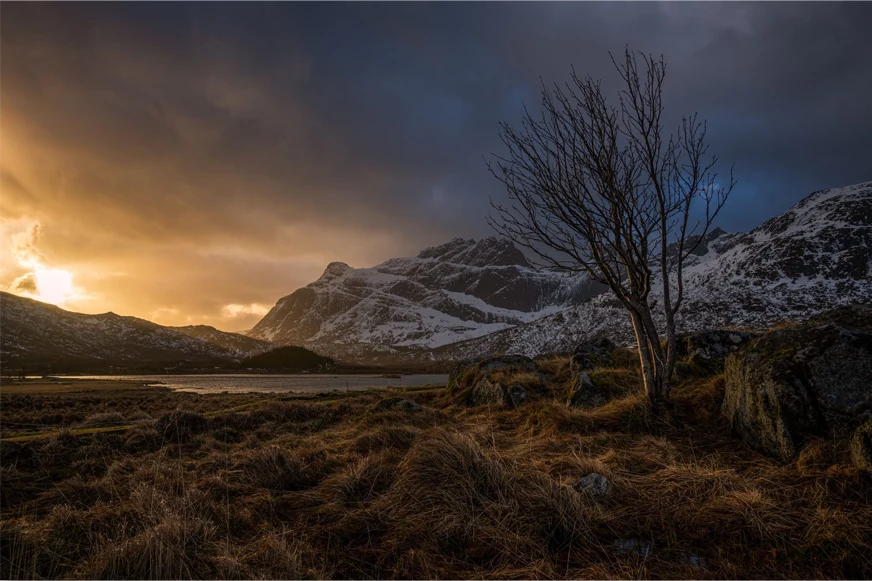A scenic view of the lake surrounded by snowy mountains during sunset